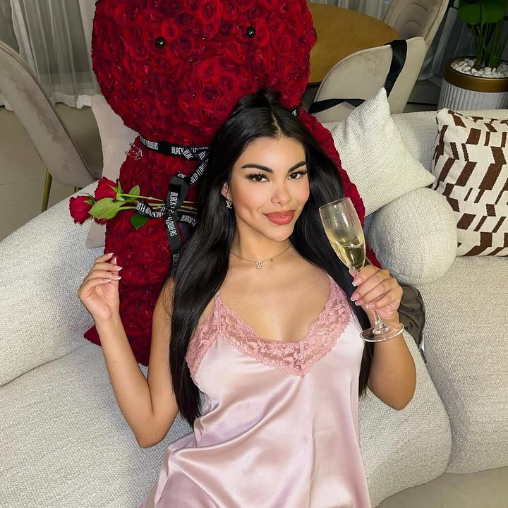 Alexandra con copa de champaña junto a un oso de rosas rojas